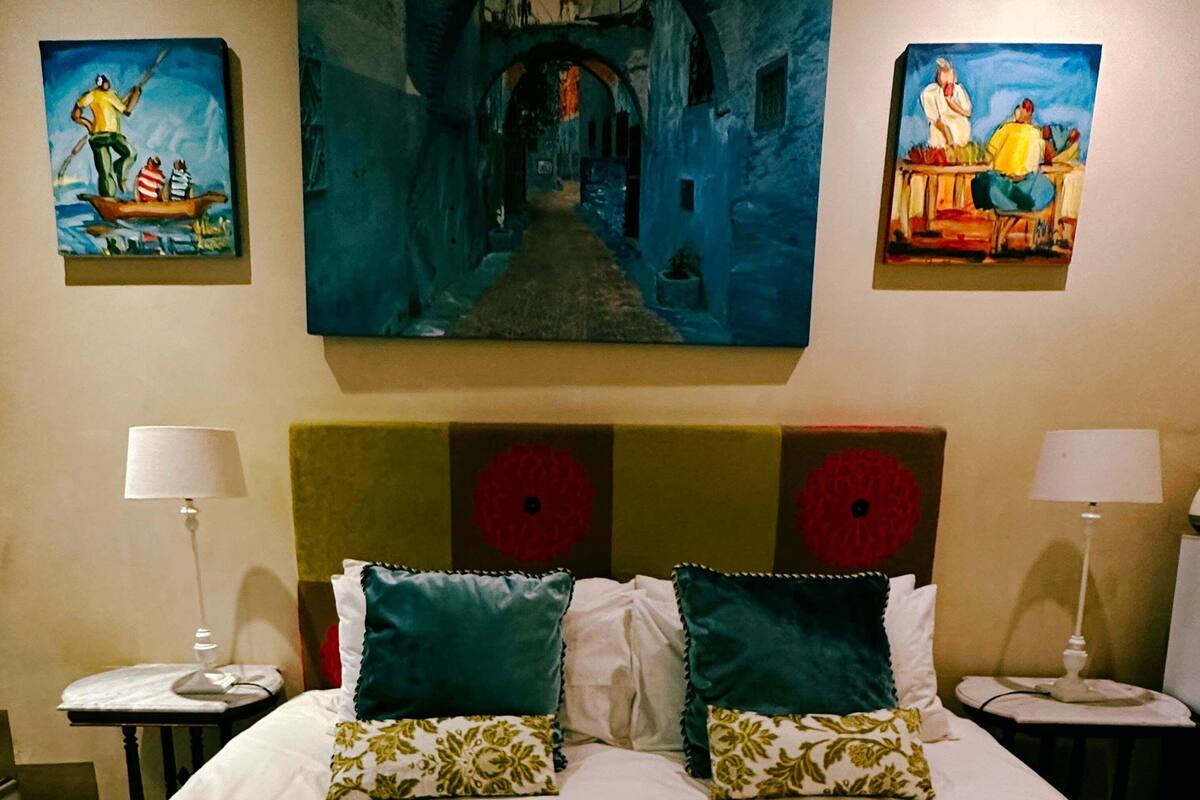 A hotel room with a large bed, two bedside tables with lamps, and three paintings on the wall.