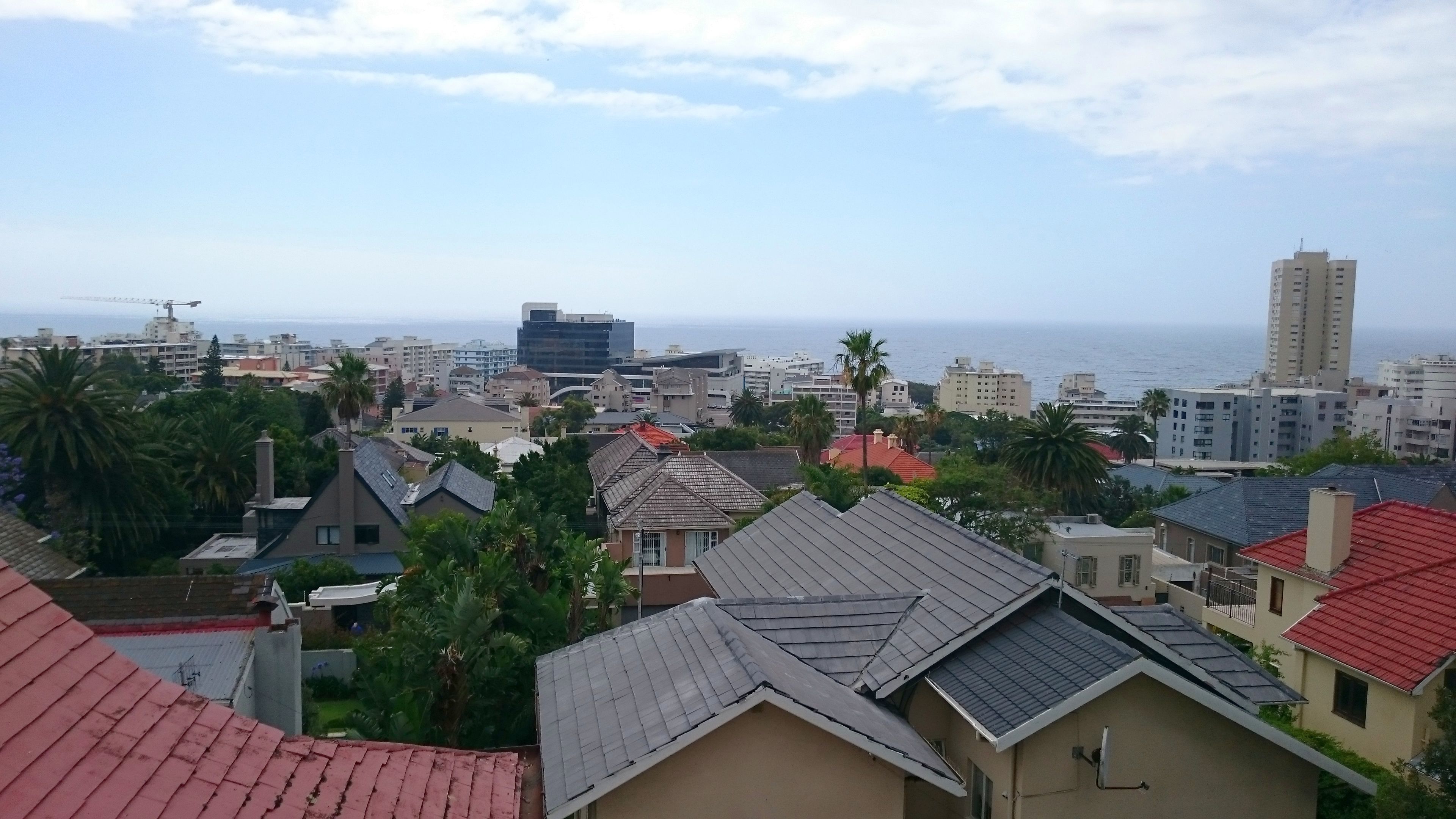 A coastal cityscape with residential buildings, some with red roofs, and a view of the sea.