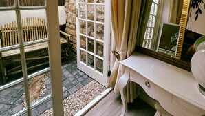 Una habitación con pared de piedra, tocador blanco con espejo y puerta que da a un espacio exterior con banco de madera.