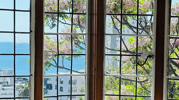 Un dormitorio con vistas al mar y flores de cerezo a través de un ventanal grande.