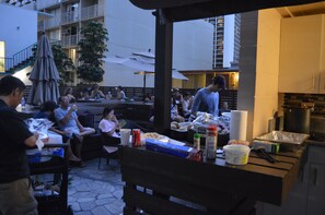 Un área de comedor al aire libre con mesas, sillas, una estación de parrillada y sombrillas para dar sombra.