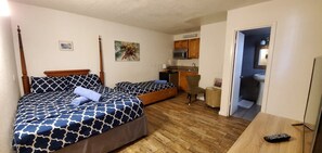 Habitación con dos camas, un escritorio, una silla, un microondas y baño visible a través de una puerta abierta.