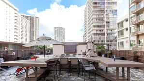An outdoor patio with a long table and chairs, surrounded by high-rise buildings.