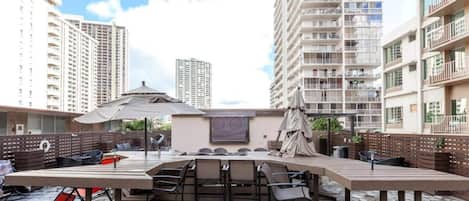 An outdoor patio with a long table and chairs, surrounded by high-rise buildings.