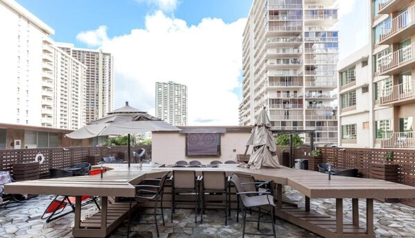 Un patio al aire libre con una mesa larga y sillas, rodeado de edificios altos.
