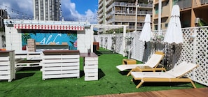 Un bar en la azotea con un mural, muebles blancos y sillones de descanso.