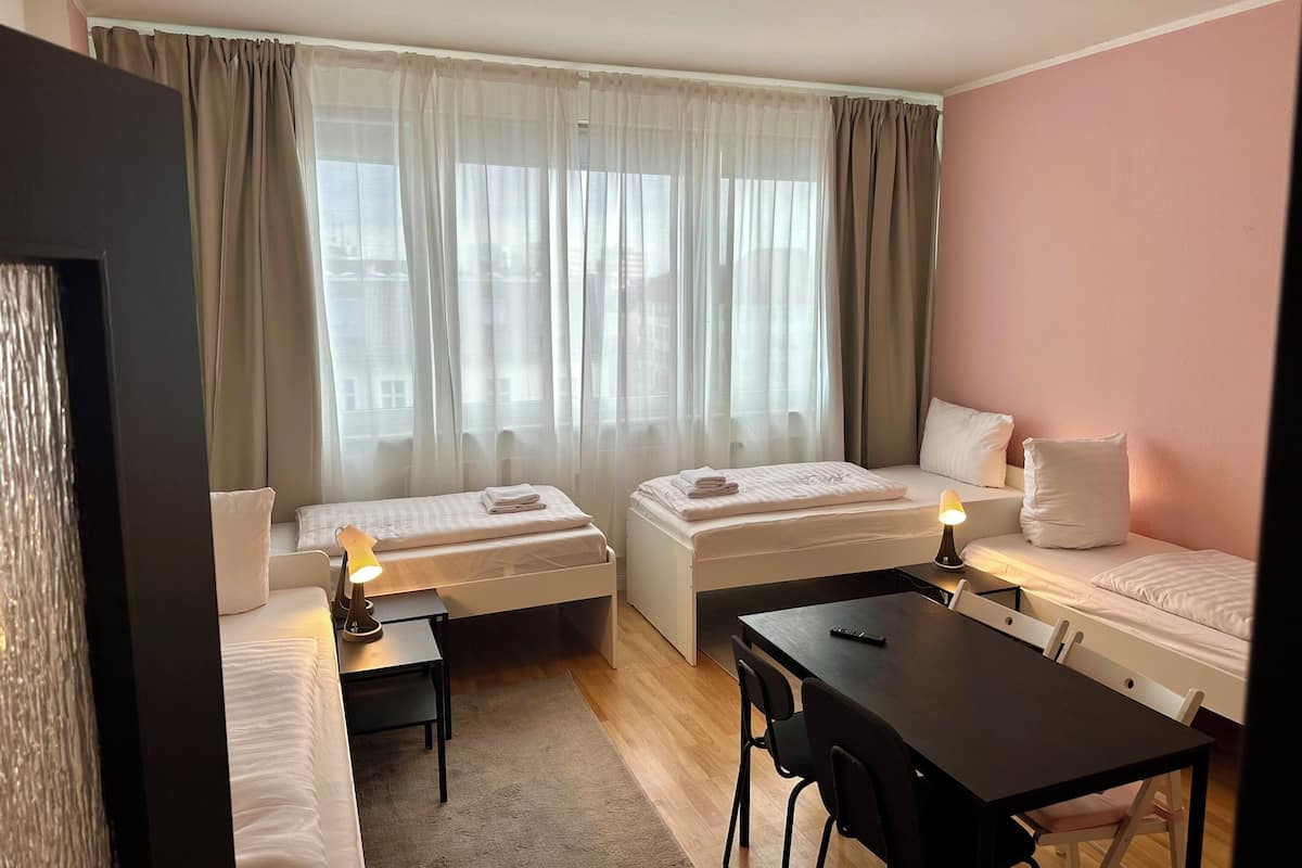 A compact hotel room with two beds, a dining table, and a small desk.