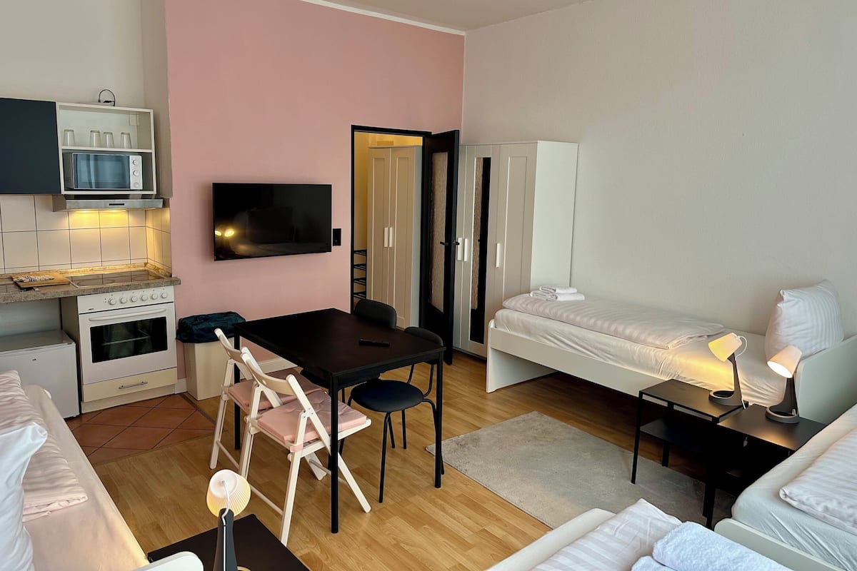 A compact hotel room with a kitchenette, a dining area, a bed, and a TV.