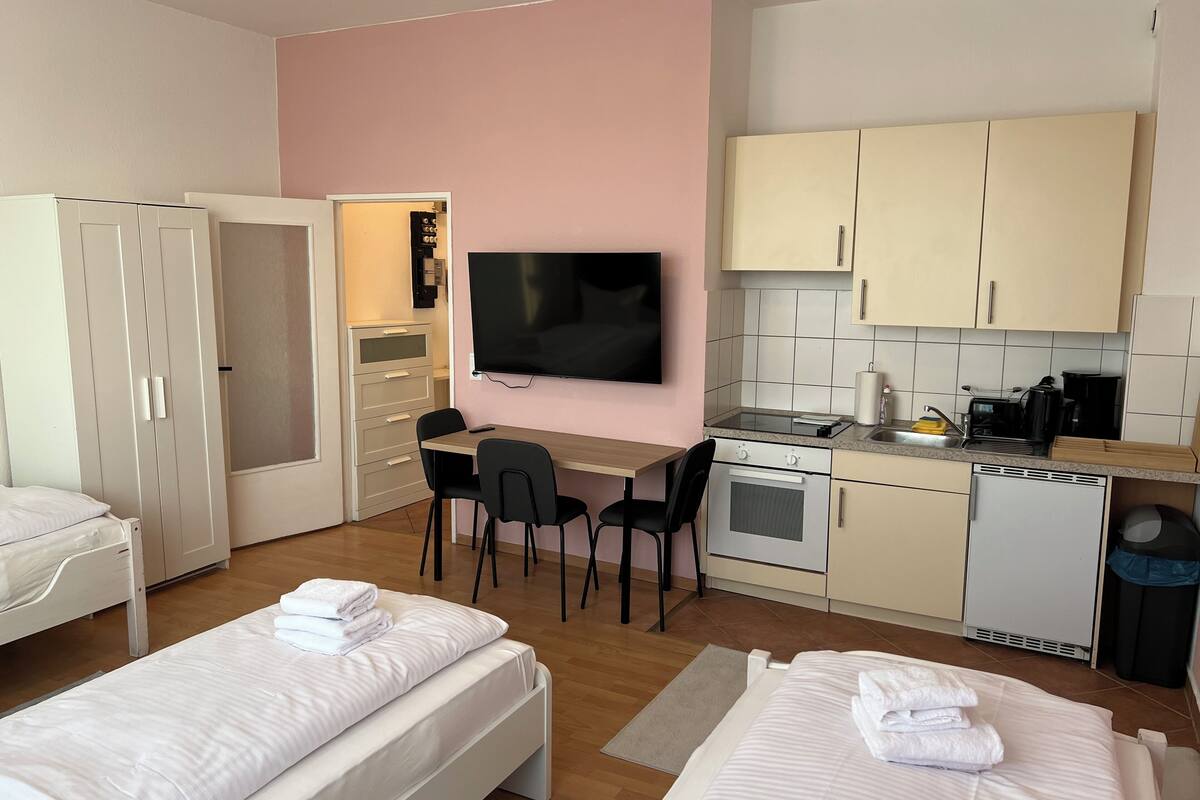 A hotel room with two beds, a desk, a TV, a kitchenette, and a wardrobe.