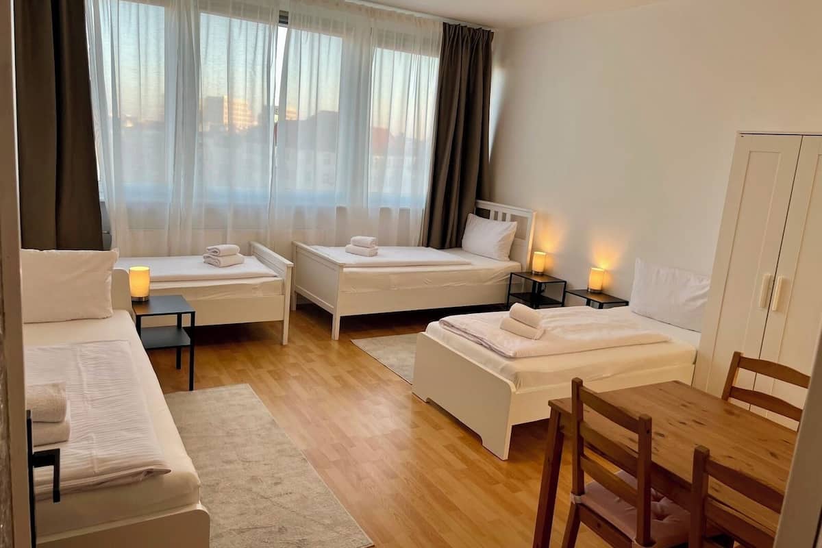 A hotel room with two single beds, a sofa, a wooden table, and a chair.