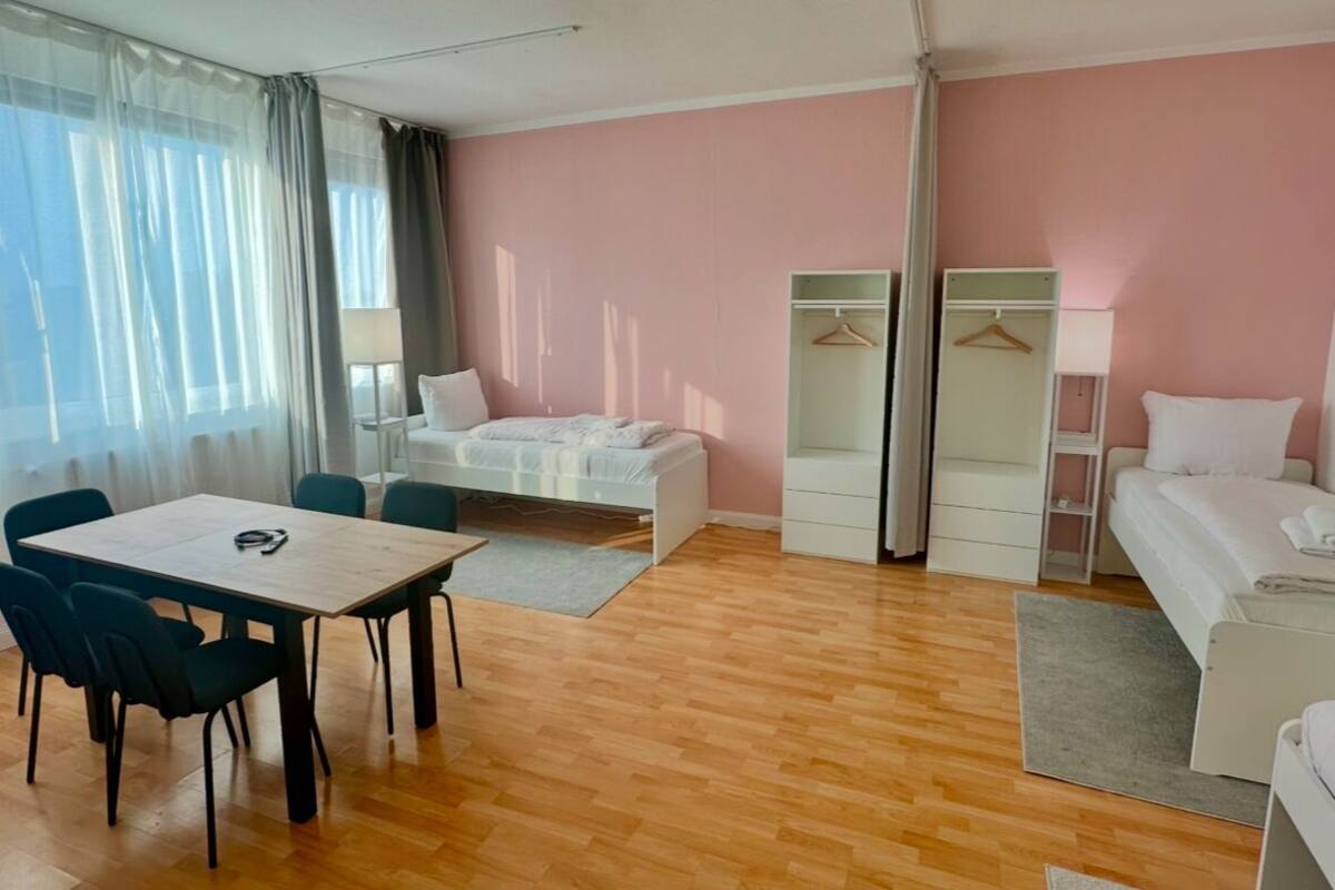 A room with a wooden floor, a bed, a desk, chairs, a wardrobe, and a hanging closet.