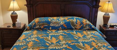 A bed with a floral bedspread, wooden headboard, two bedside tables with lamps, and wall sconces.
