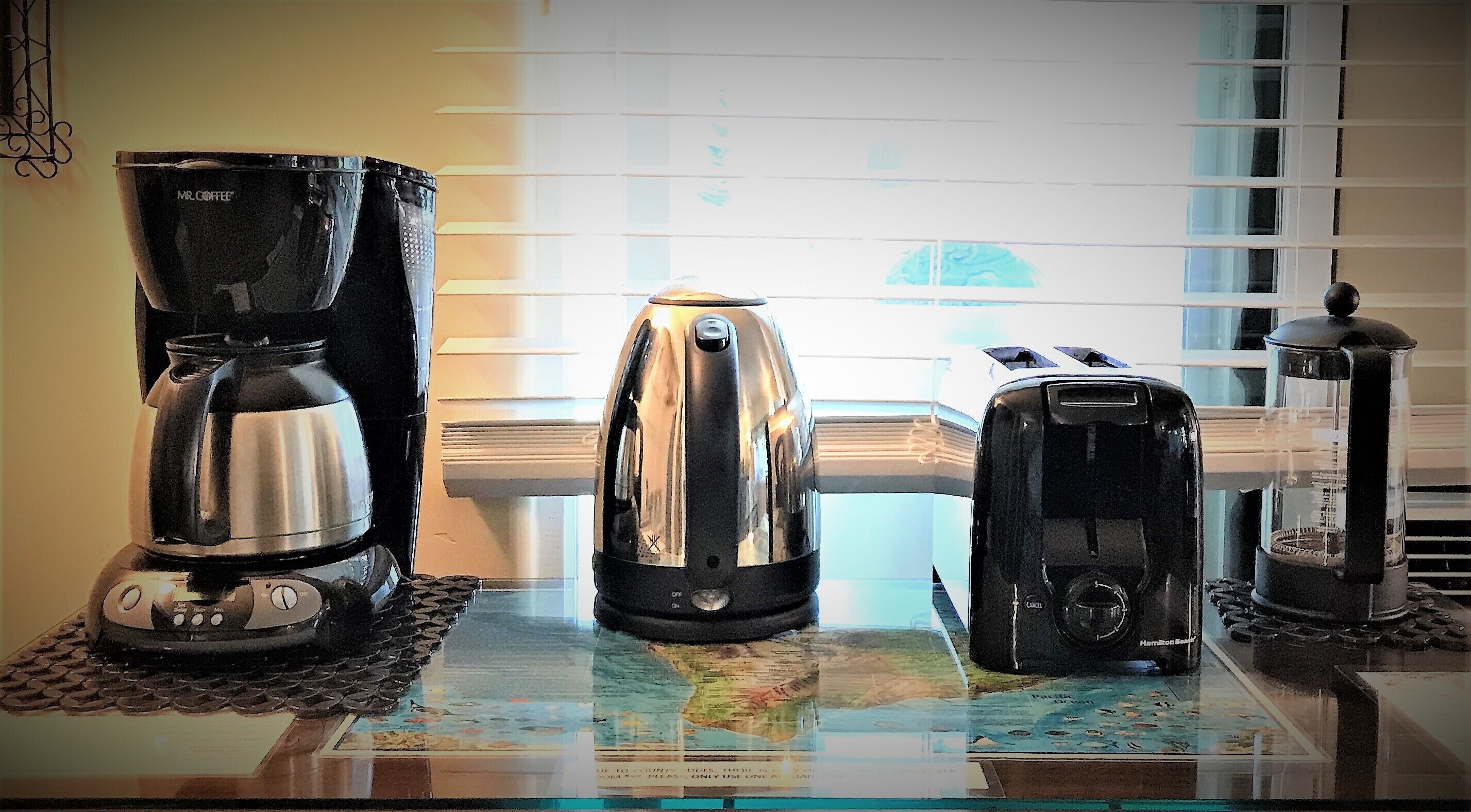 A coffee maker, a toaster, and a grinder on a table with a map underneath.