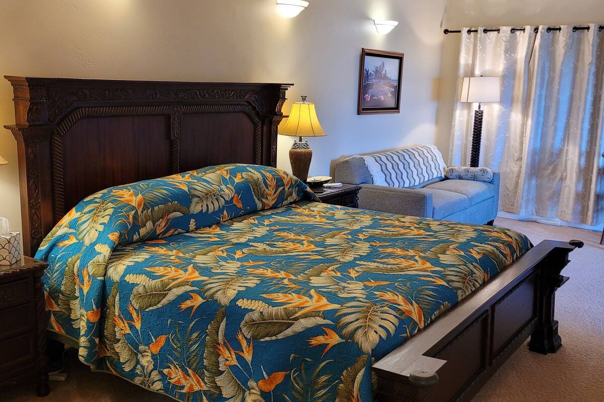 A bedroom with a large bed, a nightstand, a lamp, a sofa, and a window with curtains.