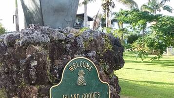 A welcome sign on a rock with a pineapple emblem, surrounded by greenery and palm trees.