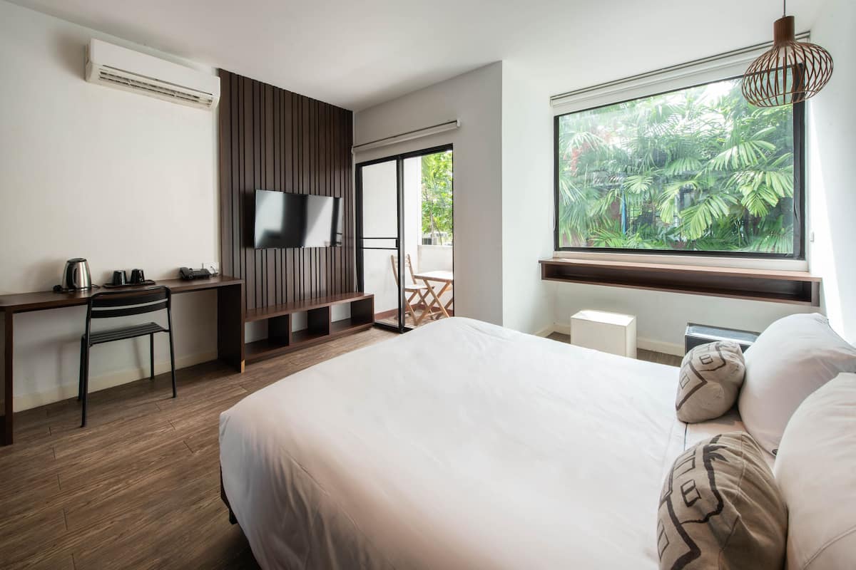 Ein Hotelzimmer mit einem Bett, einem Schreibtisch mit Stuhl, einem Fernseher und einem großen Fenster mit Blick auf Grünflächen.