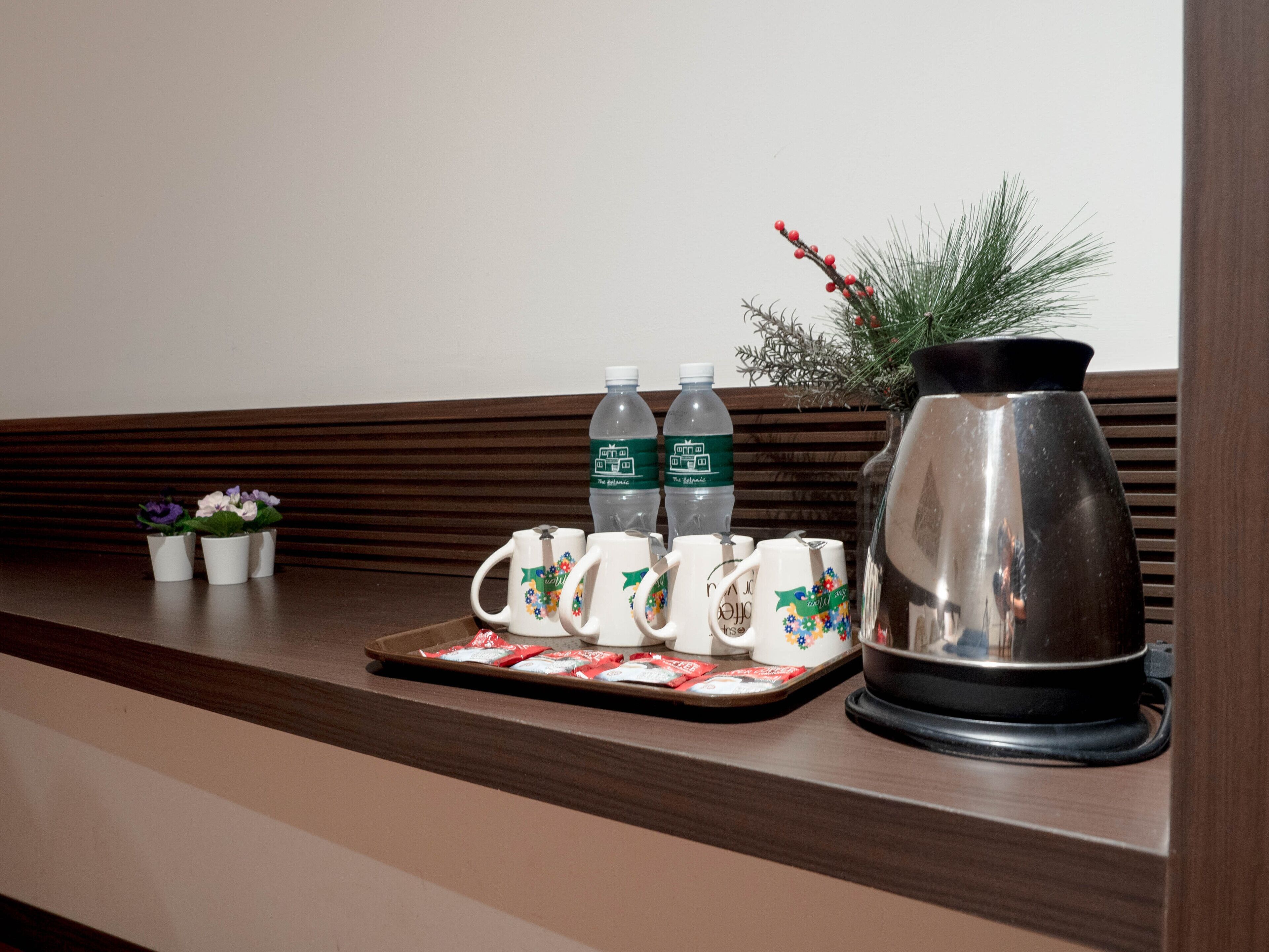Een hotel receptie met een houten balie, een dienblad met koffiemokken, twee waterflessen, een decoratieve plant en een koffiepot.
