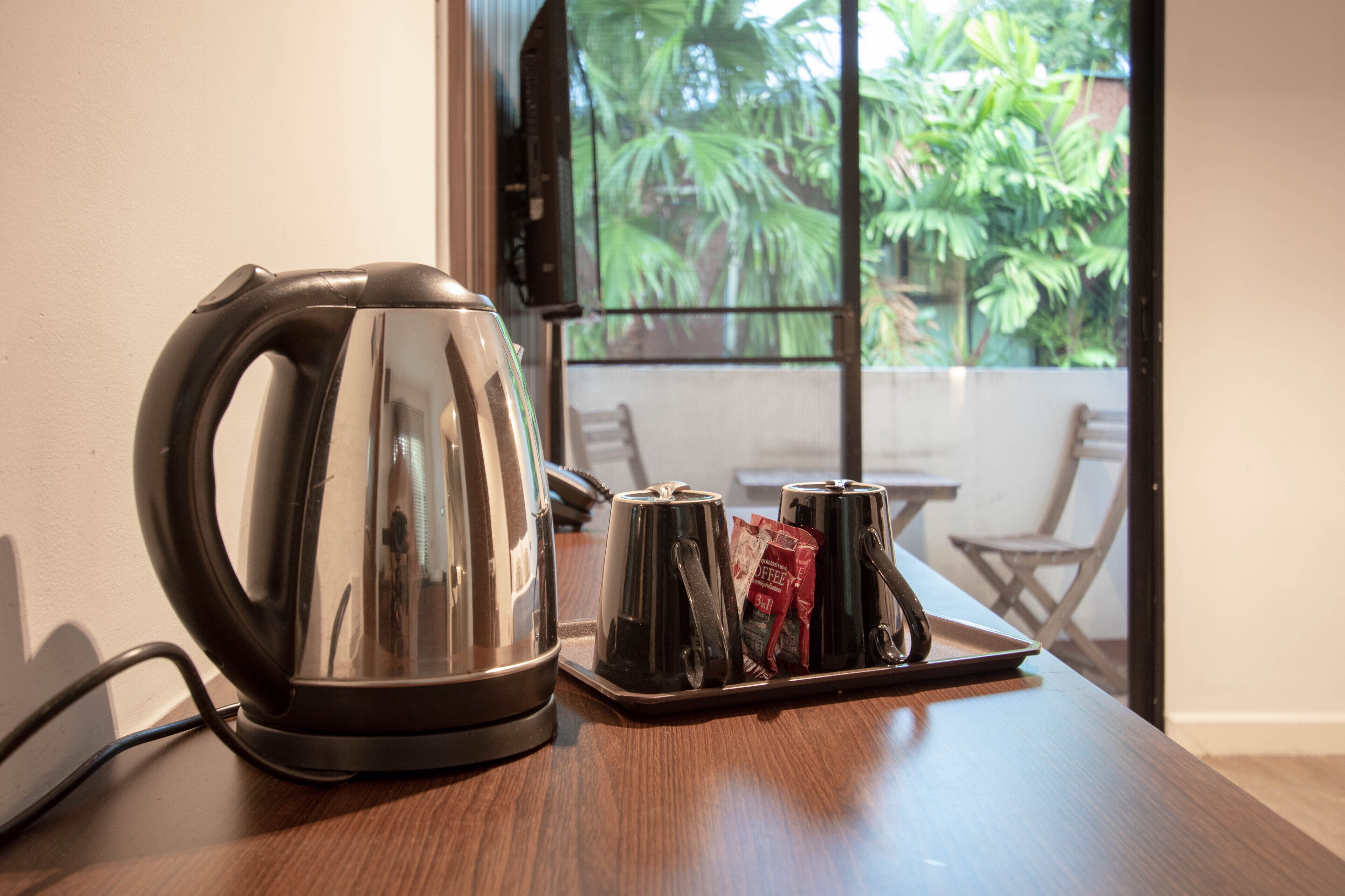 A stainless steel kettle on a tray with two cups and a coffee packet on a wooden table.