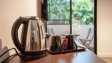 A stainless steel kettle on a tray with two cups and a coffee packet on a wooden table.