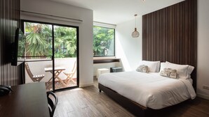A bedroom with a large bed, a desk, and a chair. There is a window with a view of greenery outside. - The Botanic Service Room (Pak Kret)