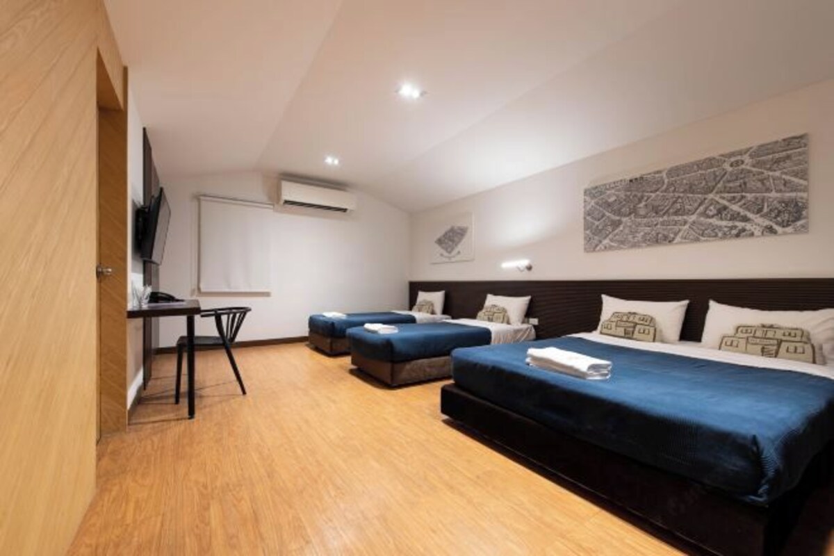 Une chambre d’hôtel avec un plancher en bois, un bureau avec une chaise, deux lits avec une literie bleue et un téléviseur fixé au mur.
