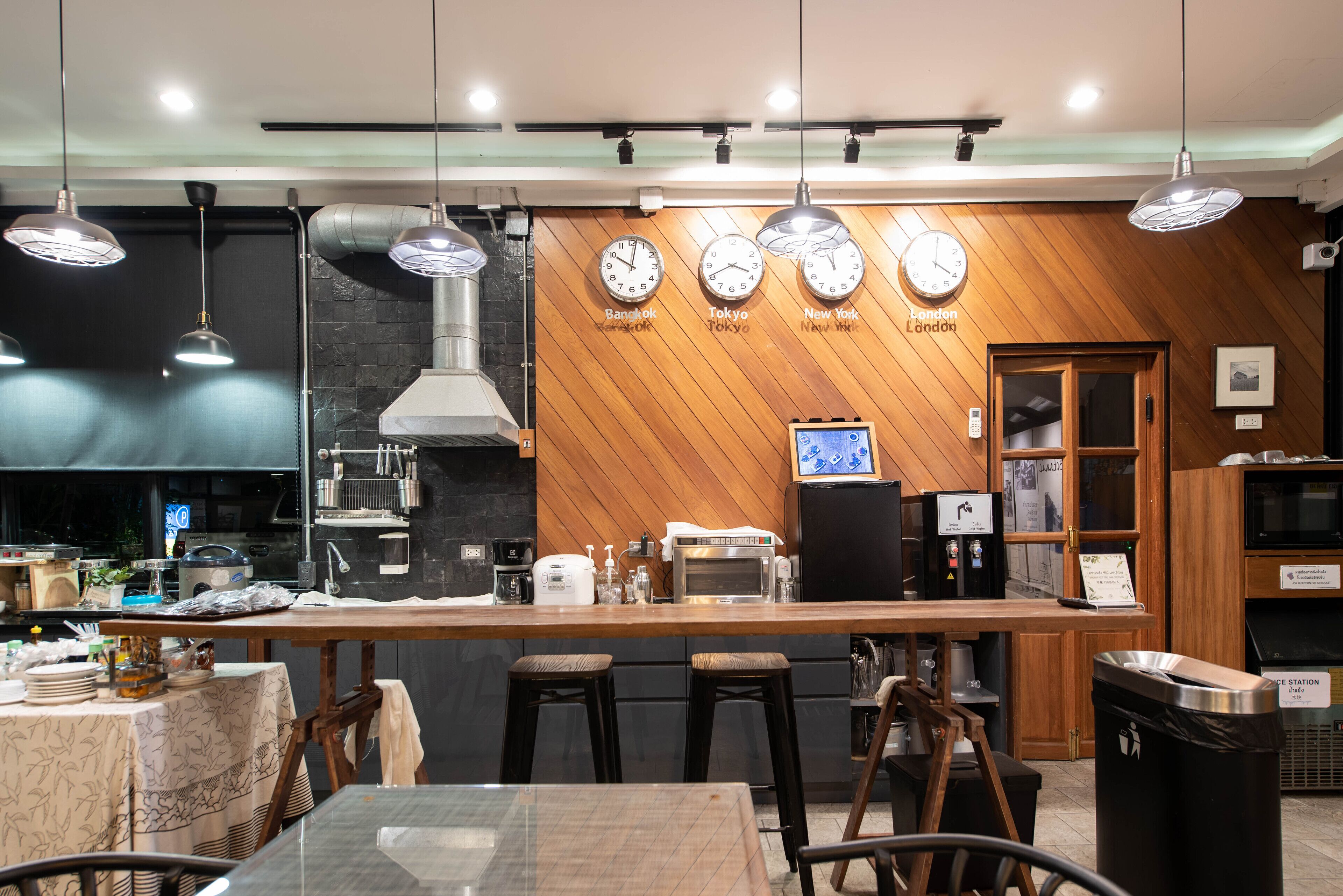 Una cocina moderna con detalles de madera, una isla central con taburetes y relojes que marcan la hora en distintas ciudades.