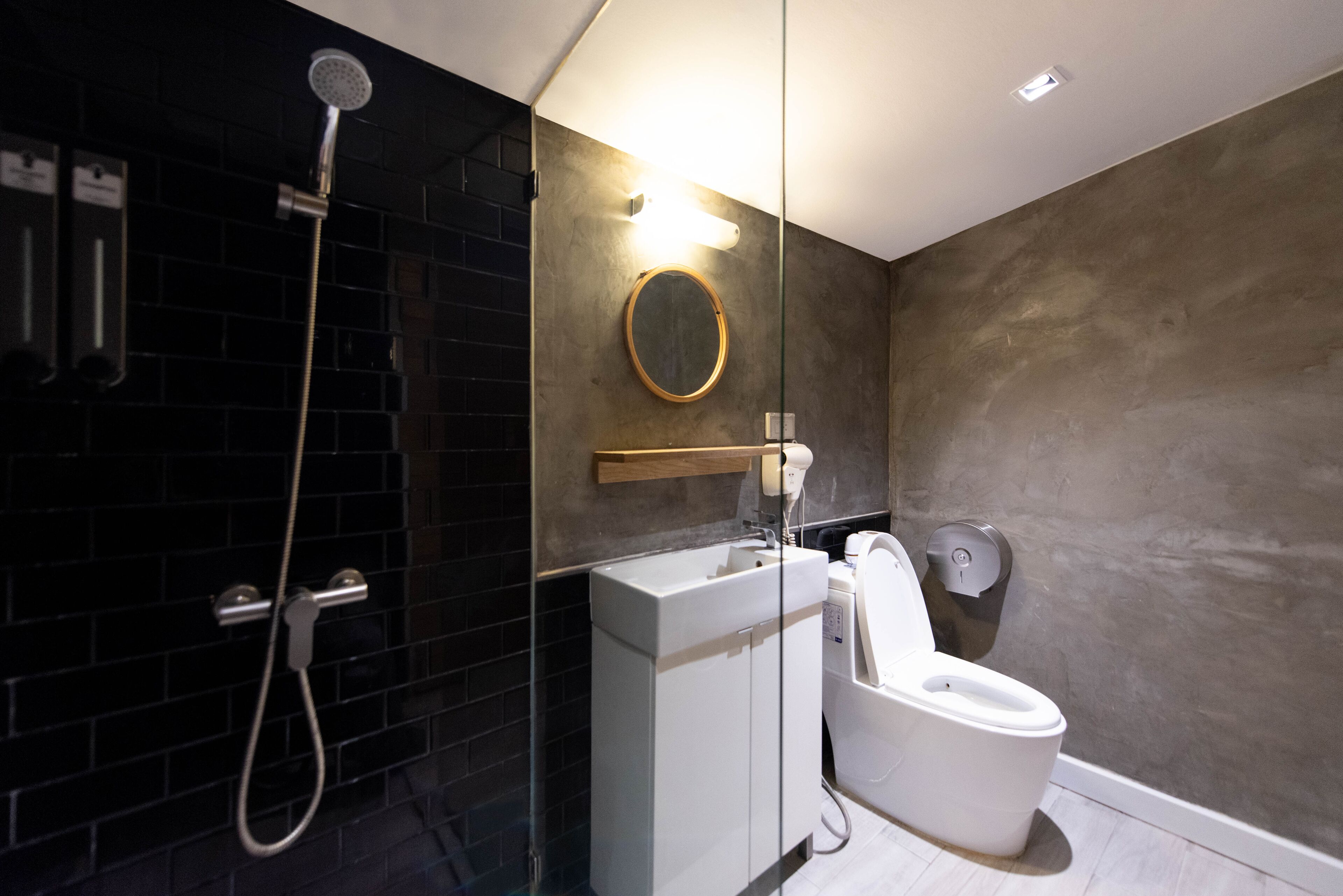 A modern bathroom with a black-tiled shower, a white toilet, and a mirror.