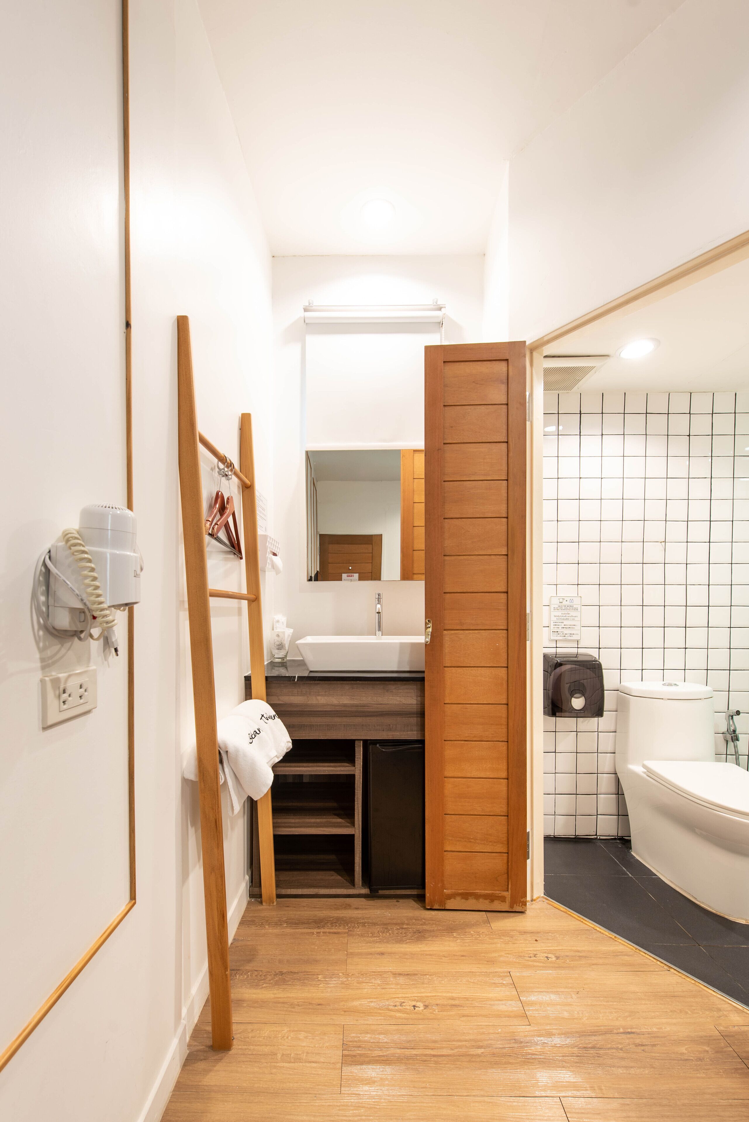 Un baño estrecho con una escalera de madera, un lavabo blanco, un espejo y una zona de ducha con azulejos.