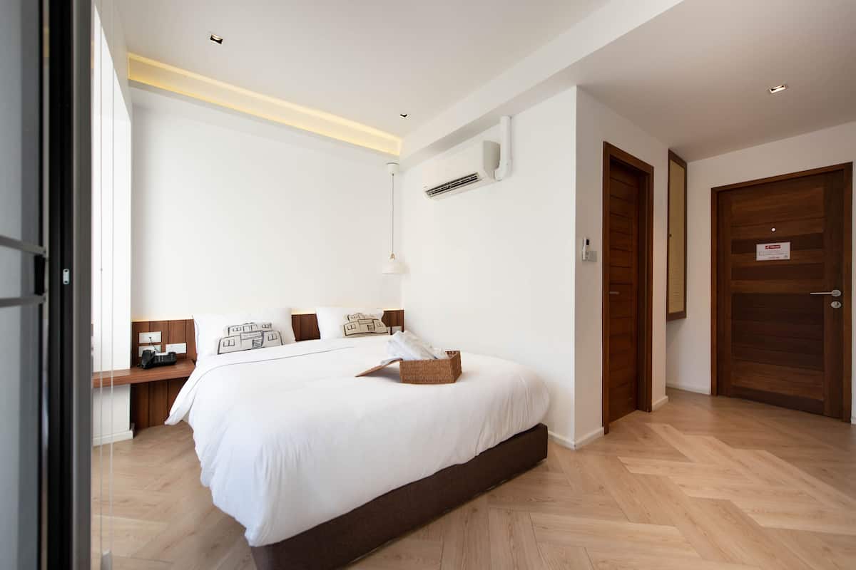 Ein modernes Schlafzimmer mit einem großen Bett, Nachttischen, einer Pendelleuchte und einer Holztür.