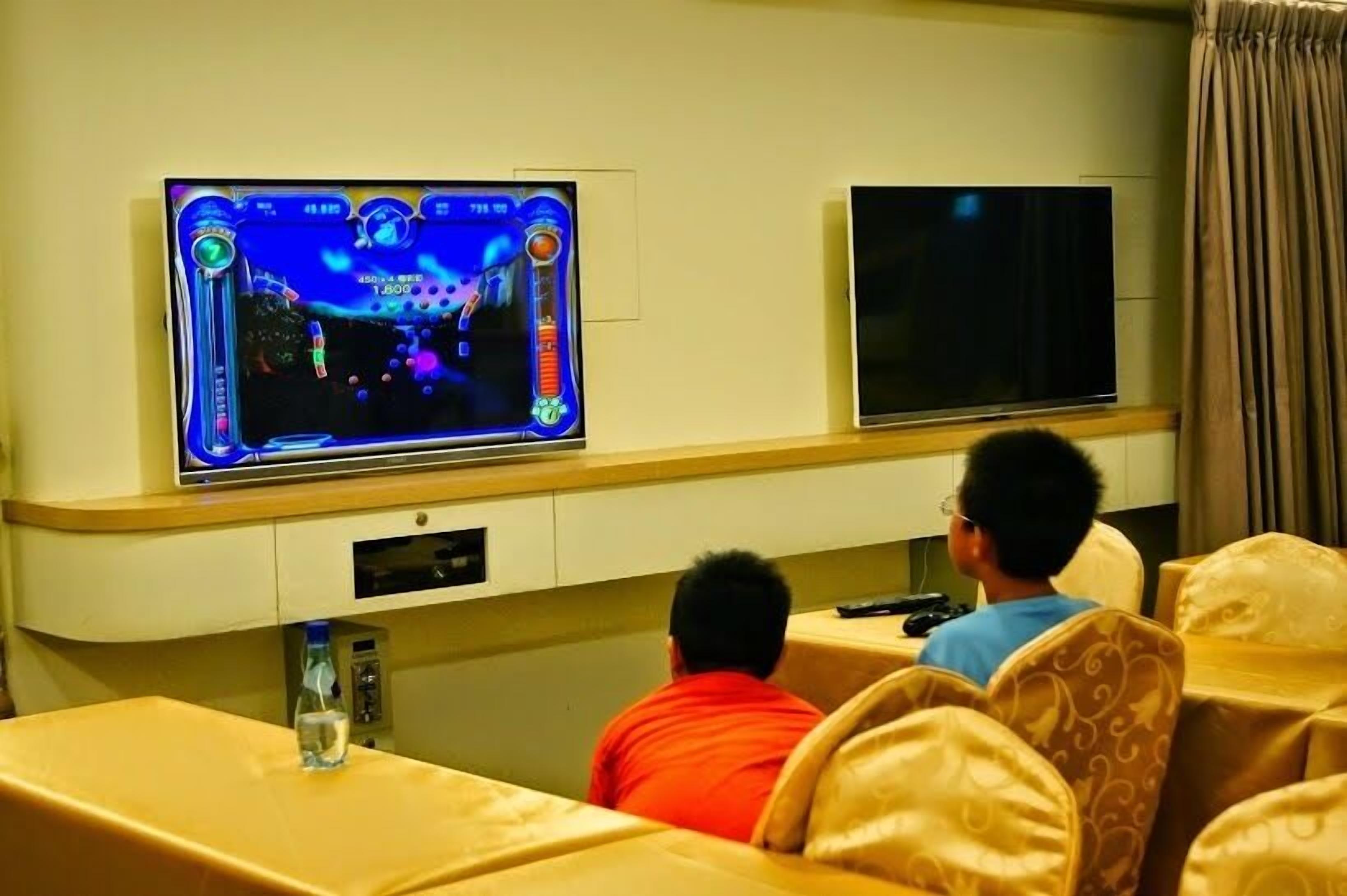 Ein Zimmer mit einem wandmontierten Flachbildfernseher, einem zweiten Fernseher an der gegenüberliegenden Wand und einem Tisch mit einer Flasche darauf.
