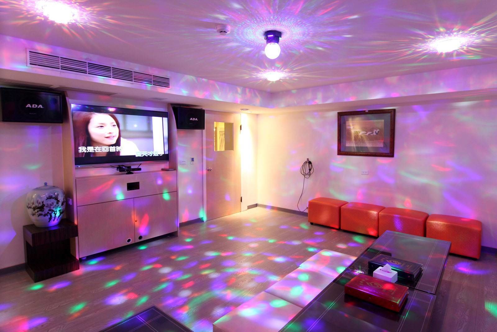 A modern room with a flat-screen TV, red seating, and colorful floor lighting.