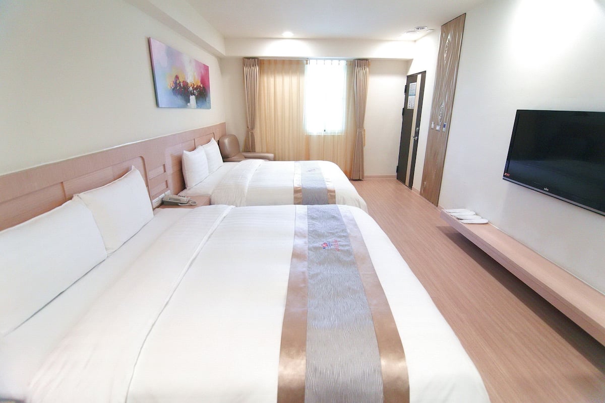 Quarto de hotel com duas camas, televisão e janela com cortinas.