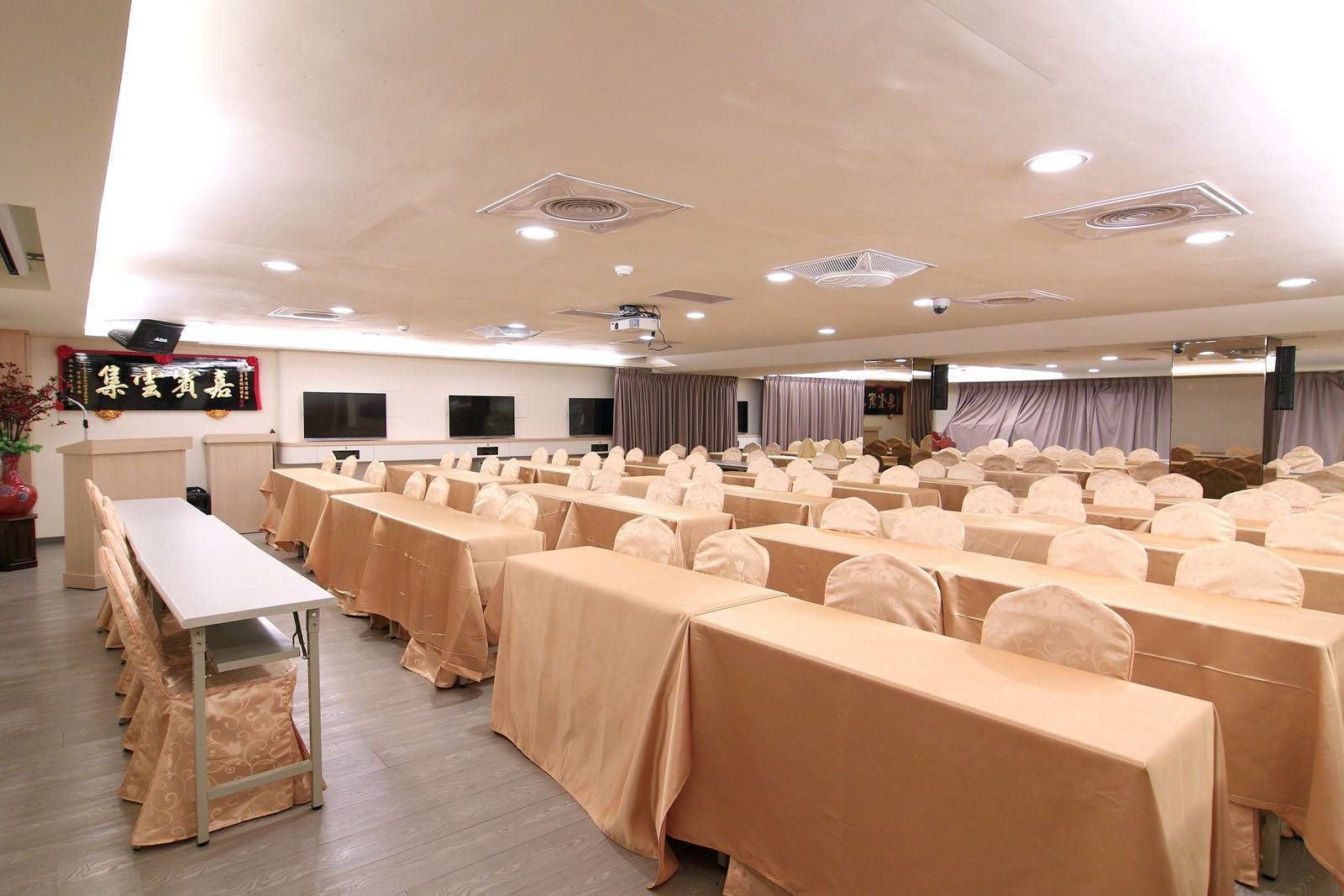 A conference room with rows of tables and chairs, a podium, and a large screen.