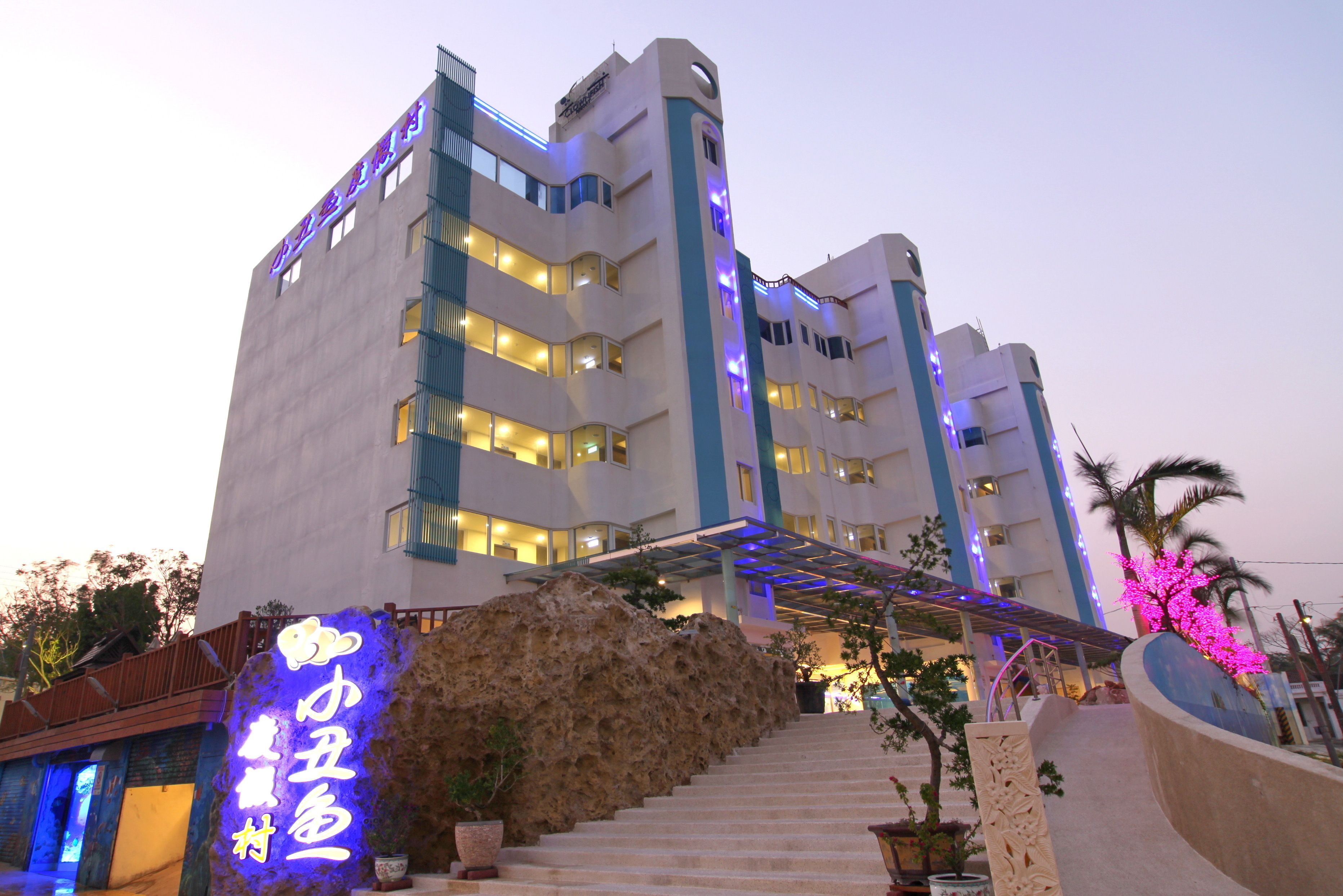 Um hotel de vários andares com design moderno, destacando uma entrada imponente com fachada de pedra e uma placa de neon.