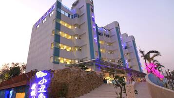Um hotel de vários andares com design moderno, destacando uma entrada imponente com fachada de pedra e uma placa de neon.