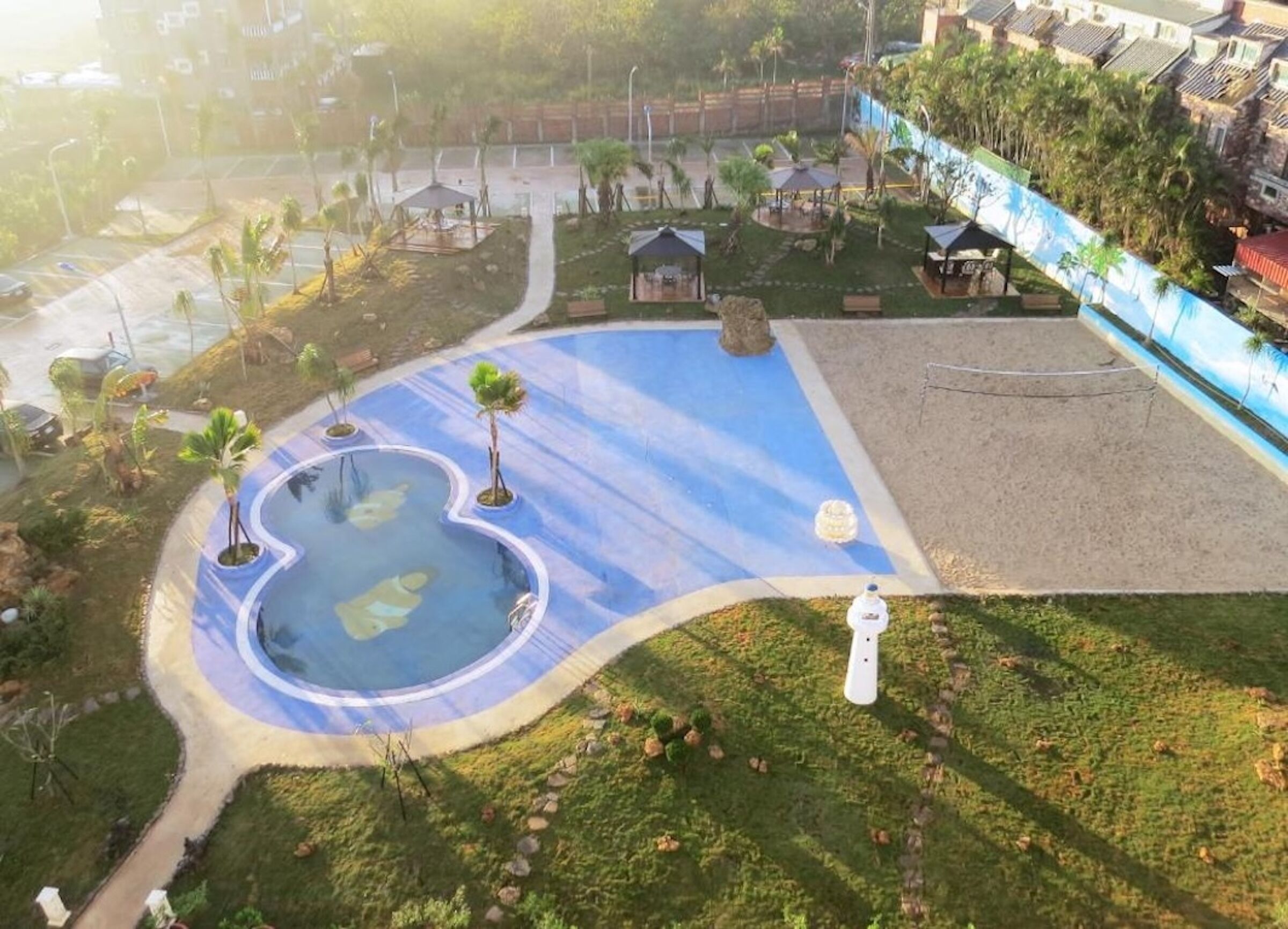 A swimming pool with a wavy edge, surrounded by grass and small trees.