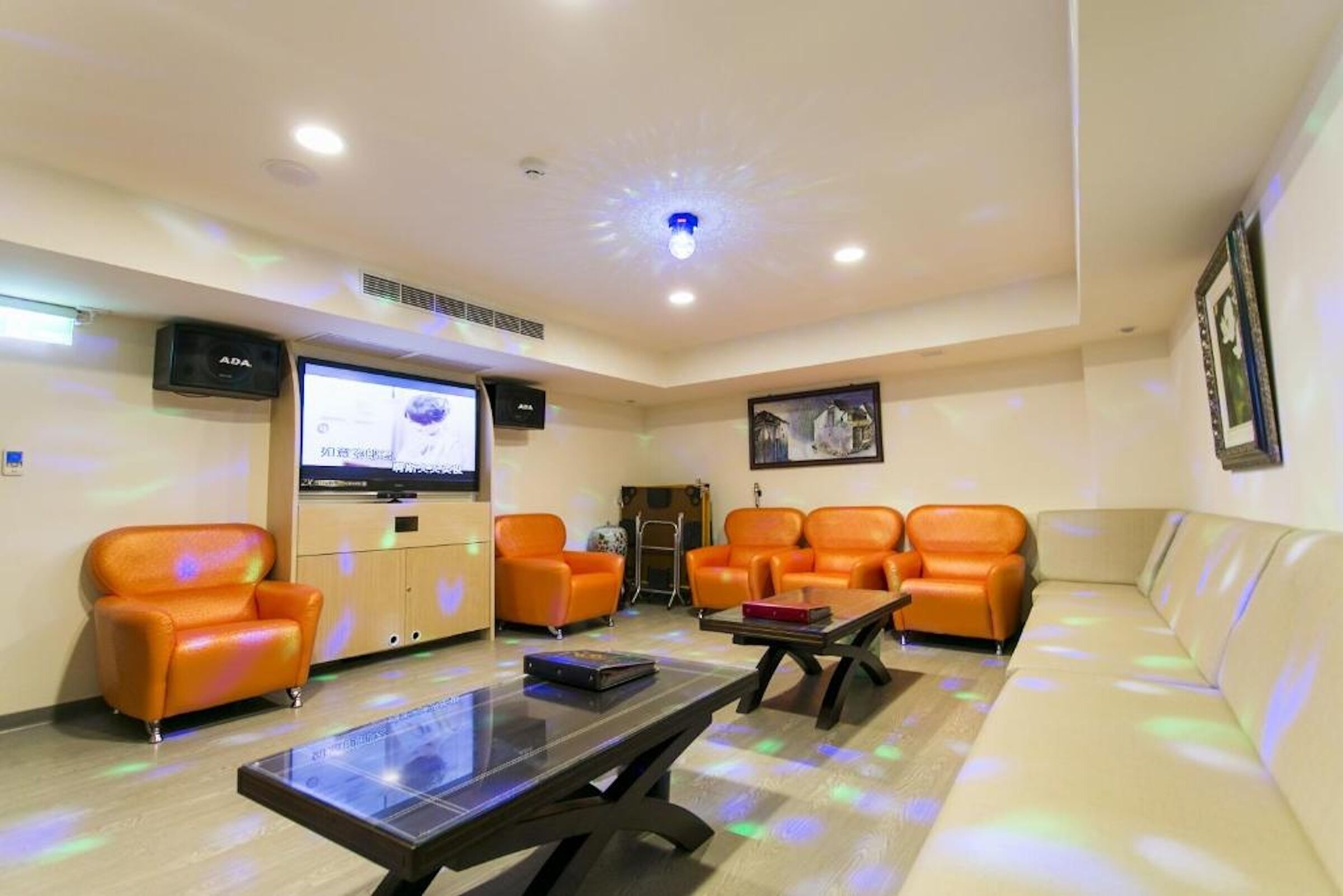 A room with orange leather sofas, a flat-screen TV, a coffee table, and a framed picture on the wall.