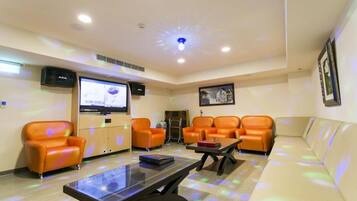 A room with orange leather sofas, a flat-screen TV, a coffee table, and a framed picture on the wall.