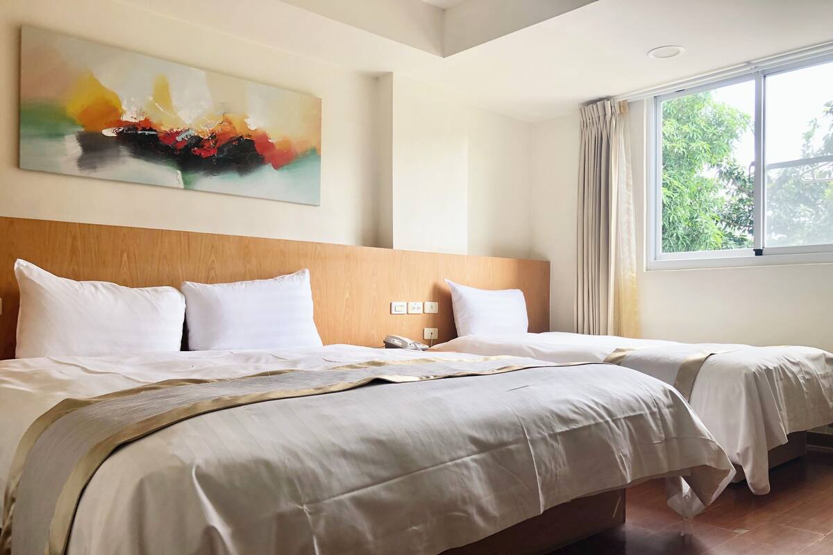 Quarto de hotel com uma cama grande, uma mesa de cabeceira, um telefone e uma janela com cortinas.