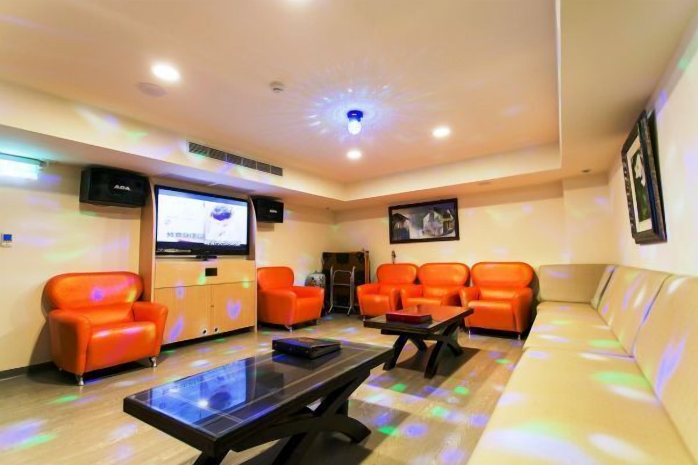Una habitación con sillones naranja, un sofá, un televisor y una lámpara en el techo.
