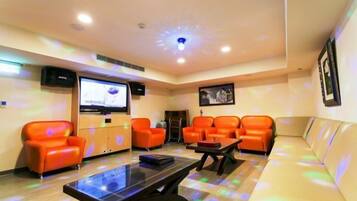 Una habitación con sillones naranja, un sofá, un televisor y una lámpara en el techo.
