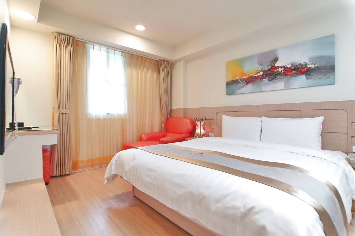 Quarto de hotel com uma cama grande, uma escrivaninha, uma cadeira e um quadro na parede.