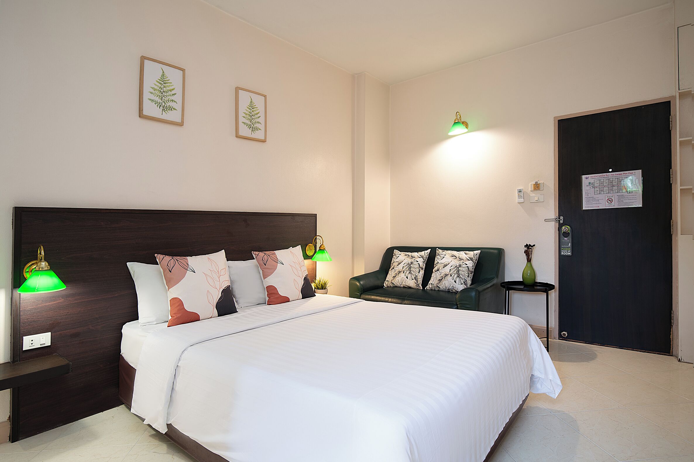 Een netjes ingerichte hotelkamer met een groot bed, twee bedlampen, een groene bank en een deur met een bordje.