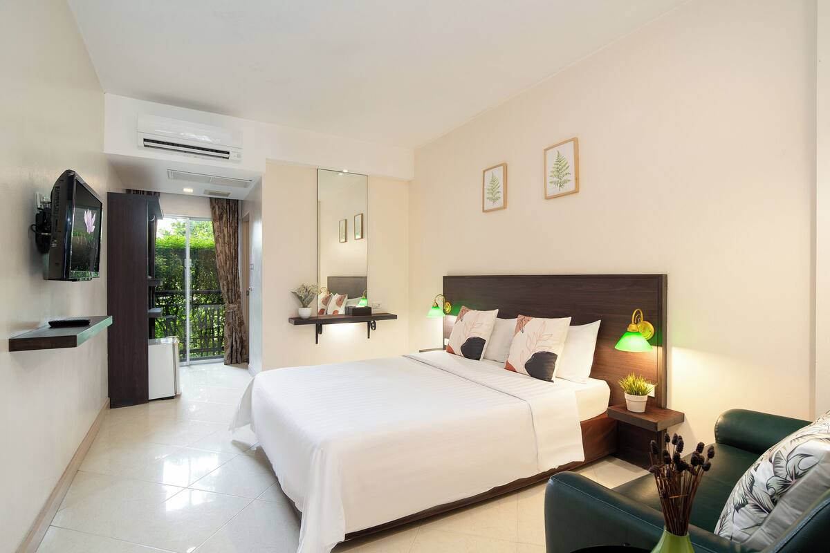 Habitación de hotel con cama, mesita de noche con lámparas, televisión, espejo y vistas a zonas verdes.