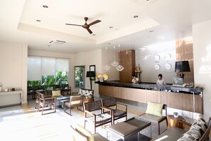 A modern hotel lobby with a reception desk, seating area, and large windows offering a view of greenery. - Synsiri Resort (Bangkok)