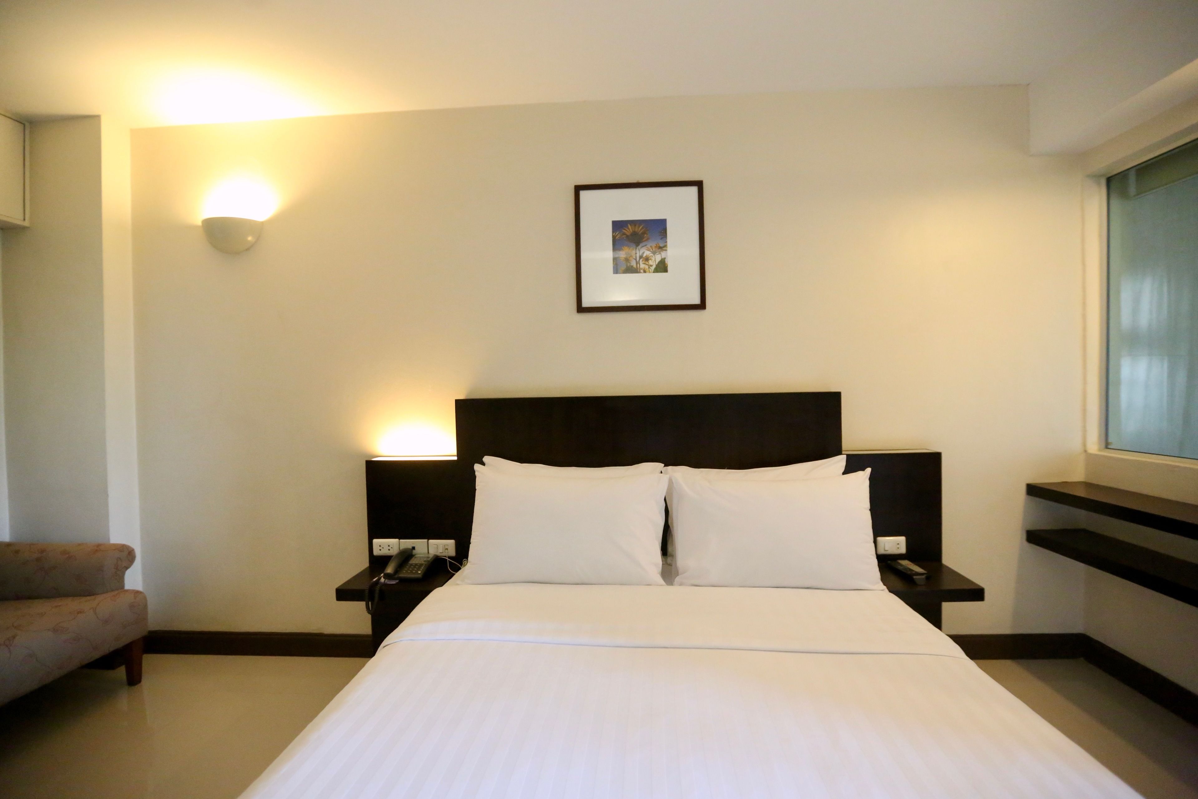 Une chambre d’hôtel avec un lit, des tables de chevet, une commode, une lampe, un tableau encadré au mur et une fenêtre.