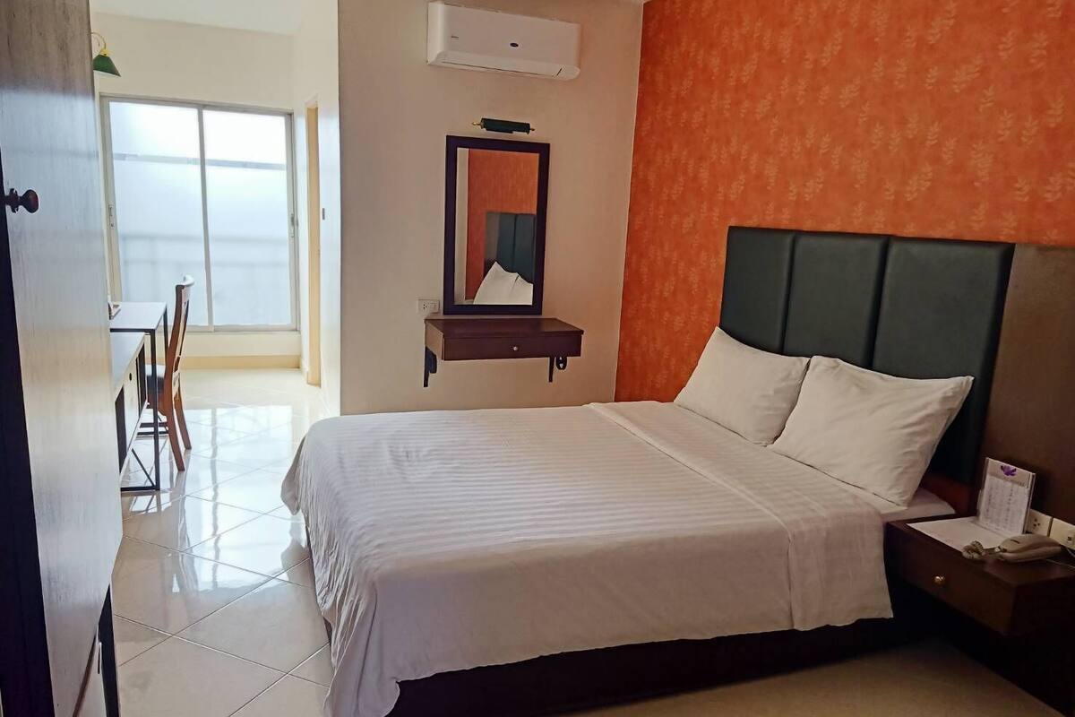 Una habitación de hotel con cama, mesita de noche, espejo y ventana.