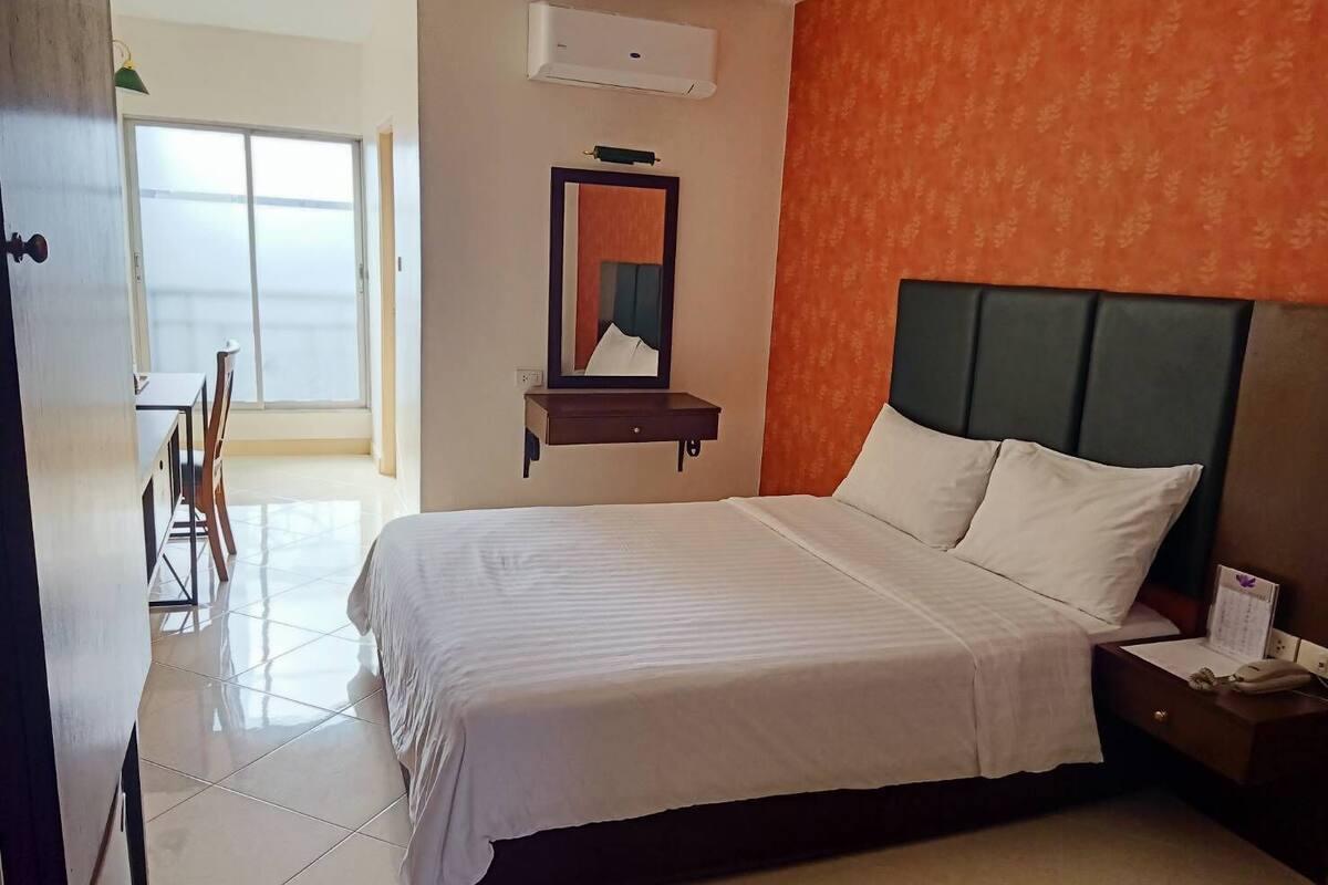 Una habitación de hotel con cama, mesita de noche, espejo y ventana.