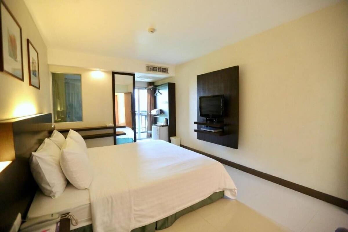Habitación de hotel con cama, televisión en la pared, espejo y puerta que da a un balcón.