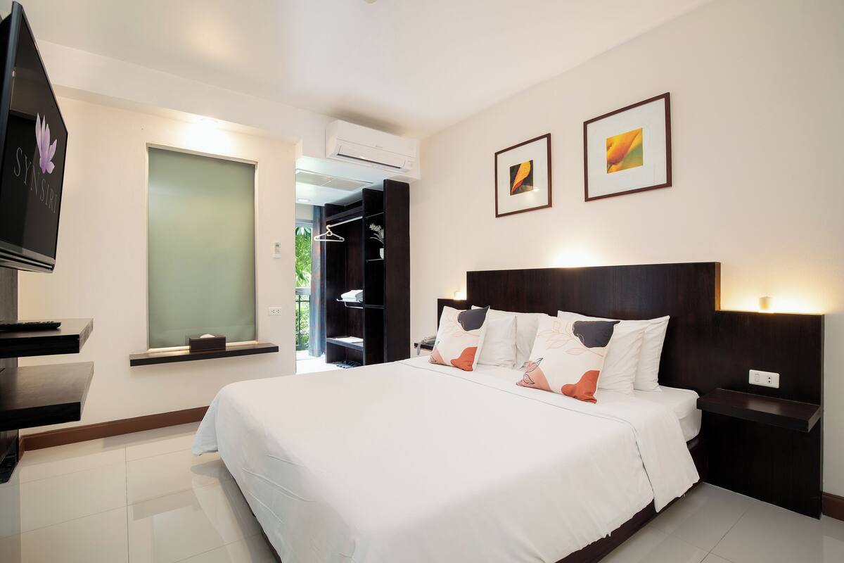 Una habitación de hotel con una cama grande, un televisor, un armario y dos cuadros en la pared.